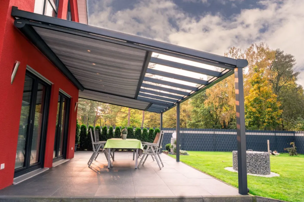 Transparente Glas-Terrassenüberdachung am roten Haus mit offener Aussicht in den Garten